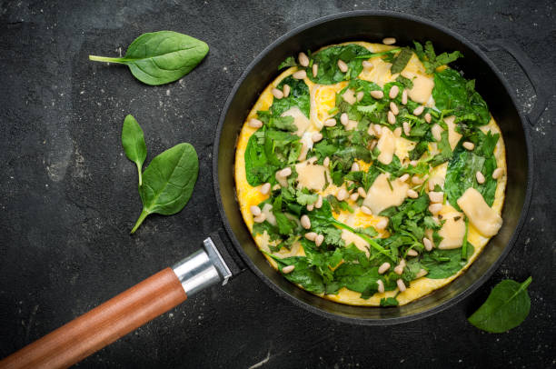 istock Omelet with eggs, spinach, pine nuts and vegetables. Spinach tortilla in pan on dark background.  Delicious breakfast or appetizer snack. Top view 825961338
