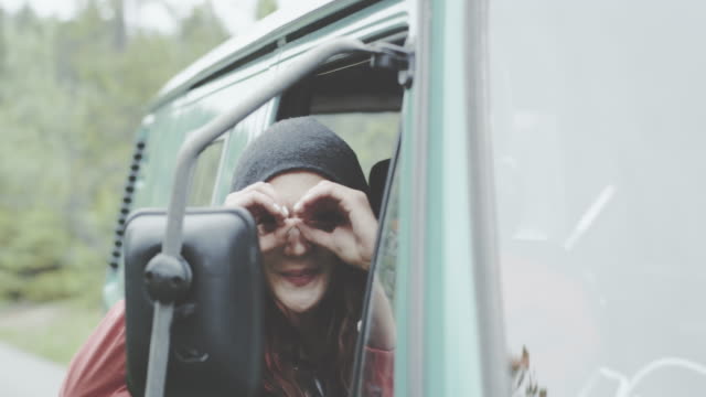 Young woman looking into car mirror and making funny faces. Sitting in a van