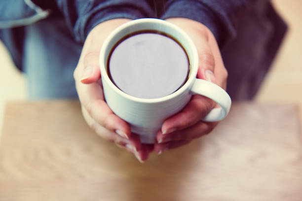istock A woman's hand holding a coffee cup on a wooden table top view 825986684