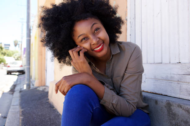 istock attractive african woman sitting on steps with mobile phone 825993086