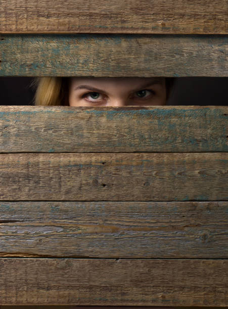 Woman watches through a hole in the wooden wall.Copy space .