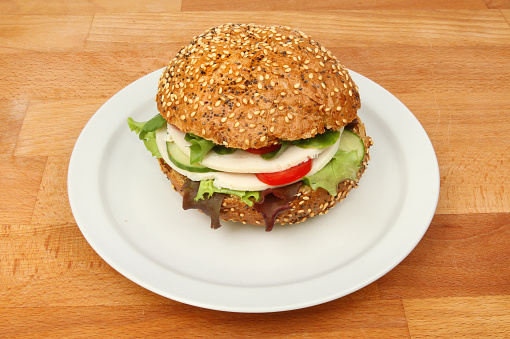 Chicken and salad in a brown bread seeded roll on a plate on a wooden tabletop