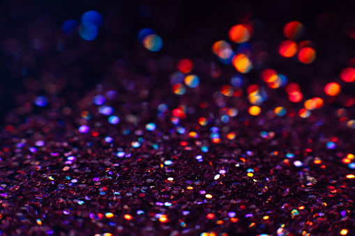 Abstract shining glitters violet holiday bokeh background with copy space. Defocused lights backdrop, selective focus with shallow depth of field. Christmas and New Year wallpaper decorations concept.