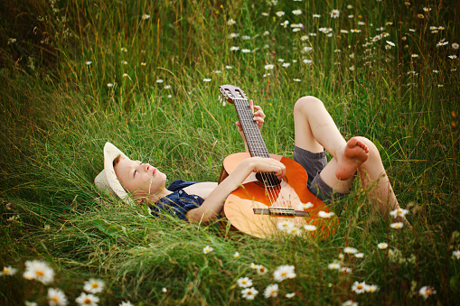 Teenage boy lying on grass with his acoustic guitar.