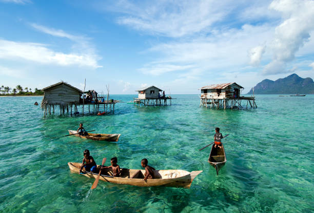 Young Bajau Laut Boy Paddling a Boat Semporna, Malaysia - 18 April, 2015: Young Bajau laut boy paddling a boat near stilted houses off the coast of Borneo in The Celebes Sea in the vicinity of Sipidan and Tun Sakaran Marine Park. mabul island stock pictures, royalty-free photos & images