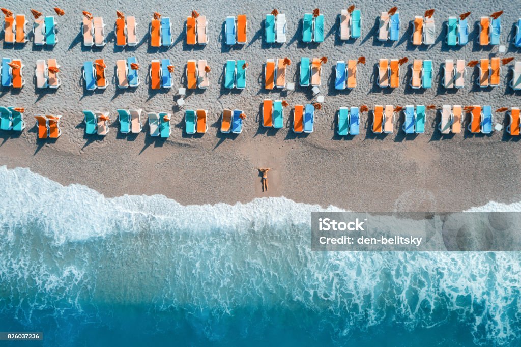 Beautiful young woman on the sea at sunrise in Oludeniz, Turkey. Aerial view of lying woman on the beach with colorful chaise-lounges. Top view from drone. Seascape with girl, azure water and waves Outdoor Chair Stock Photo