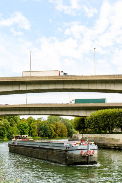 istock An empty cargo barge going down the river Marne toward Paris while semi-trailers trucks drive on the ramps of the A86 highway over the waterway. 826047344