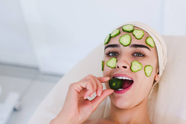 beautiful woman receibing facial mask of cucumber - facial mask spa treatment cucumber human face imagens e fotografias de stock