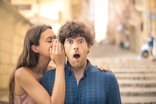 Beautiful young woman whispering a secret into her boyfriend's ear