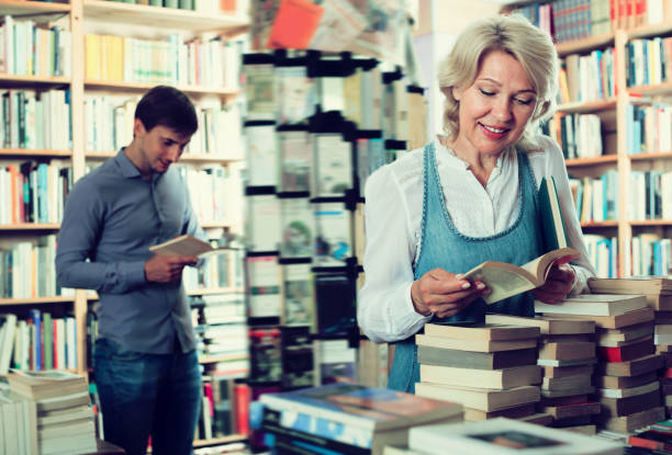 istock Glad elderly woman reading book in book shop 826109648