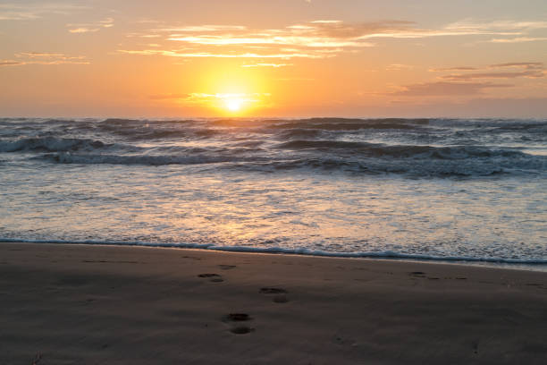 istock Sun Rising Over Calm Ocean with Foot Prints in the Foreground 826122934