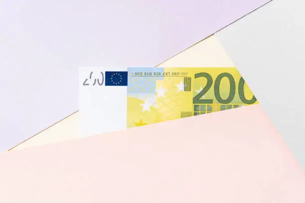 Money on pastel color block background. Two hundred euro banknote between crossing layers of yellow, purple, green, pink backgrounds.