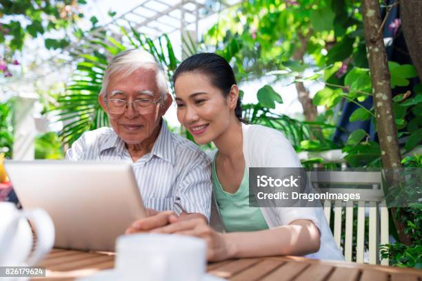 Cheerful Vietnamese Father And Daughter Sitting In Outdoor Cafe And Watching Something On Tablet Computer Stock Photo - Download Image Now