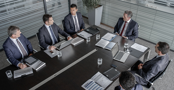 Corporate employees talking in office meeting at conference room table, side view. Businessmen and businesswoman planning business strategy, medium shot