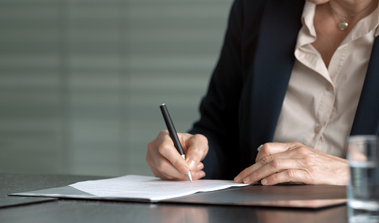 Hands of businesswoman sitting at conference table and signing contract.