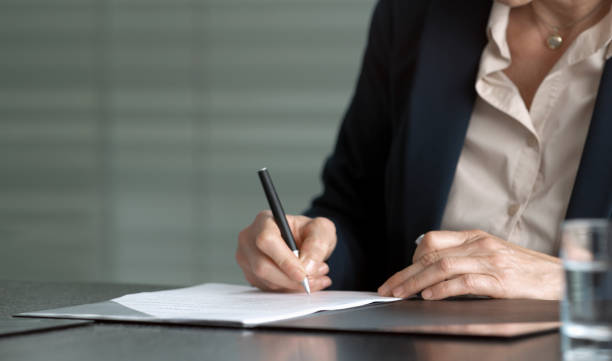 Hands of businesswoman signing contract Hands of businesswoman sitting at conference table and signing contract. pink promise stock pictures, royalty-free photos & images
