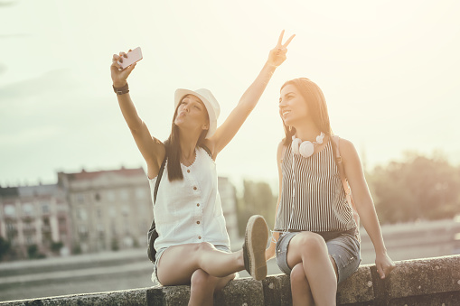 Two happy women are having fun together in the city. They are taking selfie. Intentionally toned.