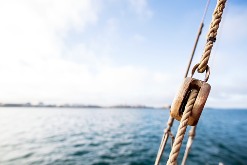 wooden pulley with a rope on a rigging vintage sailing boat with saint-malo city at the blur background during a sunny sea trip in brittany