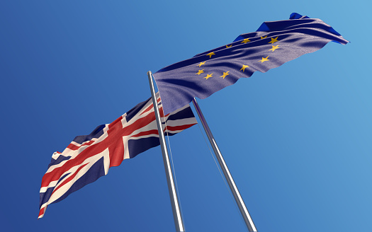 European Union and United Kingdom flags are waving with wind at opposite directions on a blue sky. Low angle view. Dispute and conflict concept. Horizontal composition with copy space. Great use for United Kingdom and European union related concepts.