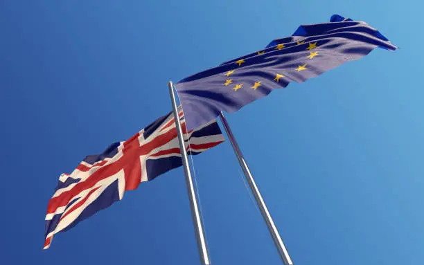 European Union and United Kingdom flags are waving with wind at opposite directions on a blue sky. Low angle view. Dispute and conflict concept. Horizontal composition with copy space. Great use for United Kingdom and European union related concepts.