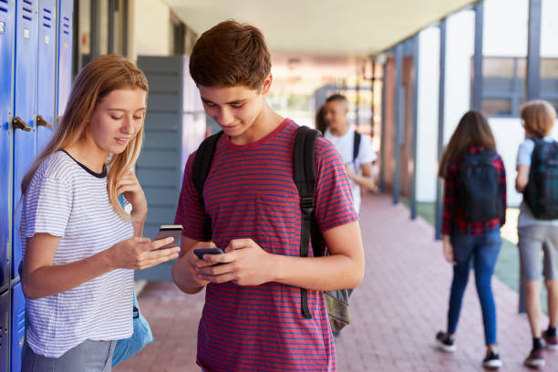 istock Two friends talking and using phones in school corridor 826212016