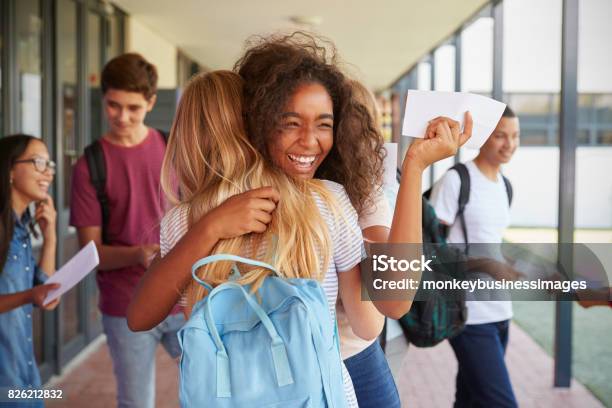 Dos Chicas Celebrando Los Resultados De Los Exámenes En Corredor De Escuela Foto de stock y más banco de imágenes de Adolescente