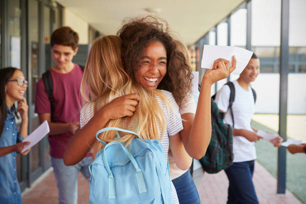 Two girls celebrating exam results in school corridor Two girls celebrating exam results in school corridor three quarter length photos stock pictures, royalty-free photos & images