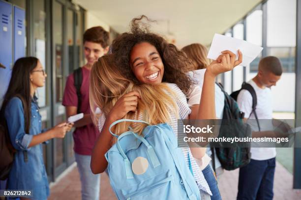 Two Girls Celebrating Exam Results In School Corridor Stock Photo - Download Image Now