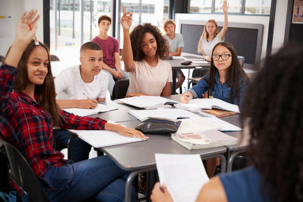 high school kids raise hands, teacher sitting at their desk - multi ethnic group concentration student asian ethnicity imagens e fotografias de stock