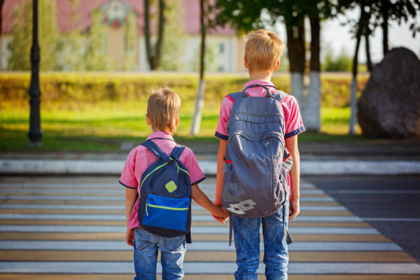 istock Two kids with backpacks walking on the road, holding. School tim 826235628