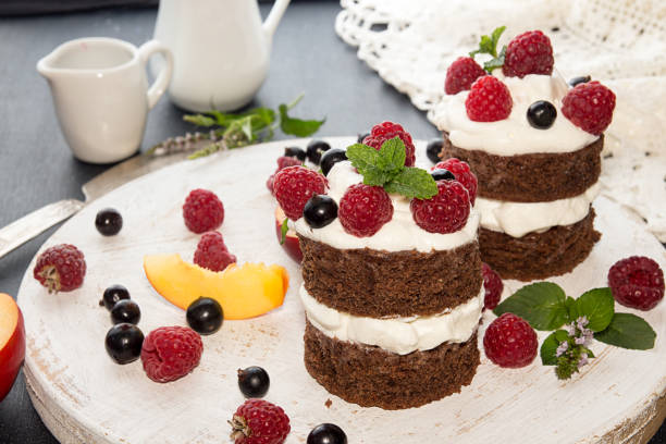 chocolate cake decorated with raspberry, black currant, nectarine, wipped cream and mint on white wooden board - wipped cream imagens e fotografias de stock