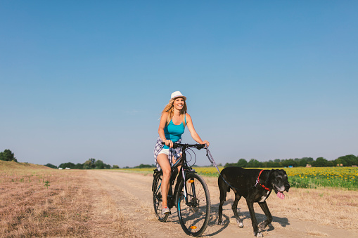 Mid adult woman with her dog, great dane. She is riding her bike and her dog is running next to her.