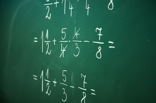 Calcualting with fractions on green blackboard at primary school