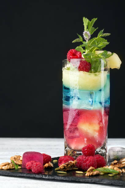 istock Close-up of fresh multi-colored cocktail with raspberry, pineapple, ice and crushed walnuts on a black background. Copy space. 826267654