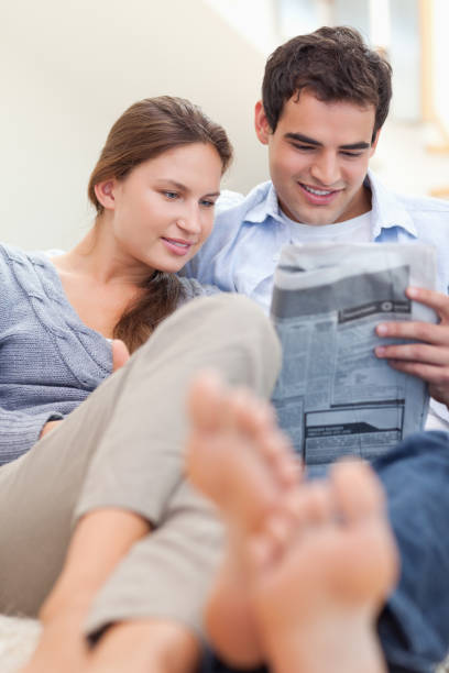 istock Portrait of a couple reading a newspaper while lying on a couch 826268382