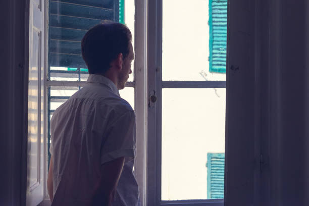 istock A man looking out window from a dark room 826268416