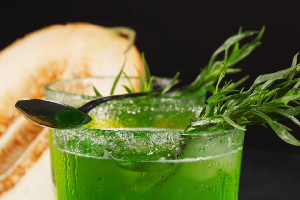 nahaufnahme eines estragon trinken. ein glas grün alkoholischen cocktail mit einem löffel. kalten pflanzliches getränk und melone auf einem schwarzen hintergrund. - tarragon close up freshness herb stock-fotos und bilder