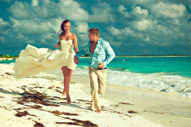 istock Newly married bride and groom is running along coastline. Wedding on the beach. 826285218