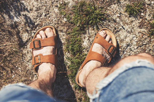Top view of male legs in brown leather sandals and blue jean shorts Top view of male legs in brown leather sandals and blue jean shorts, standing on a rocky trail sandal stock pictures, royalty-free photos & images