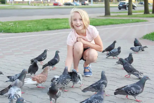 Photo of Cheerful girl feeds pigeons on the street in the city