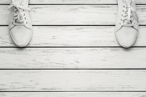 Youth classic white leather sneakers on wooden whute background.