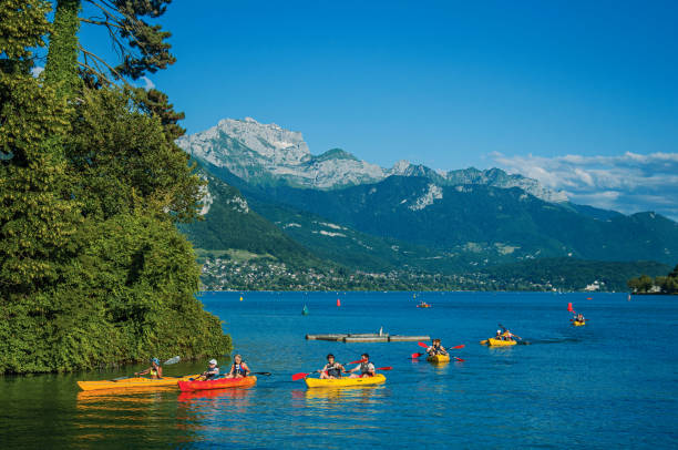 annecy lake with island, vegetation, kayaks, peaks and blue sky in annecy - loch rowboat lake landscape imagens e fotografias de stock