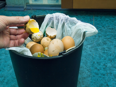Human hand throwing bad egg into a rubbish bin, filtered photo