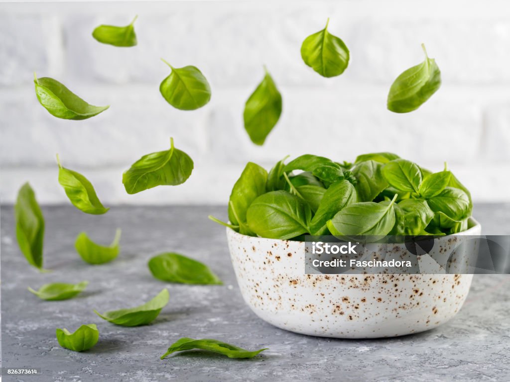 Fly shpinach over kitchen table Flying fresh green basil leaves and bowl with spinach on gray table and white brick wall background. Fly spinach. Cooking pesto and raw food concept. Basil Stock Photo