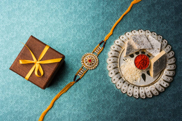 Raksha Bandhan - Rakhi and gift with sweet kaju katli or mithai and rice grains and kumkum in a decorative plate. Traditional Indian wrist band which is a symbol of love between Brothers and Sisters. Raksha Bandhan - Rakhi and gift with sweet kaju katli or mithai and rice grains and kumkum in a decorative plate. Traditional Indian wrist band which is a symbol of love between Brothers and Sisters. rakhi stock pictures, royalty-free photos & images