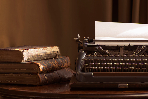 Vintage portable typewriter with a piece of paper and vintage books on a table in brown tones