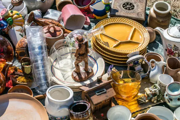 pile of household things, various dishes and decorative objects at boot sale for second hand, recycling or over-consumption society at outdoor welfare