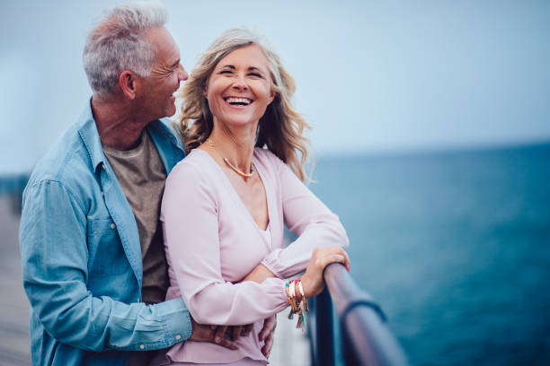 married senior couple having fun, laughing and relaxing at seaside - looking at view water sea blue imagens e fotografias de stock