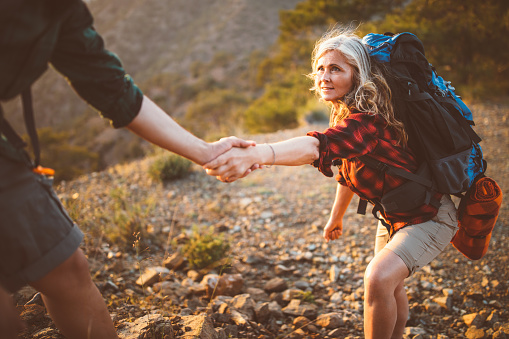 Active senior woman hiker on ecotourism holidays holding helping hand to climb on mountain