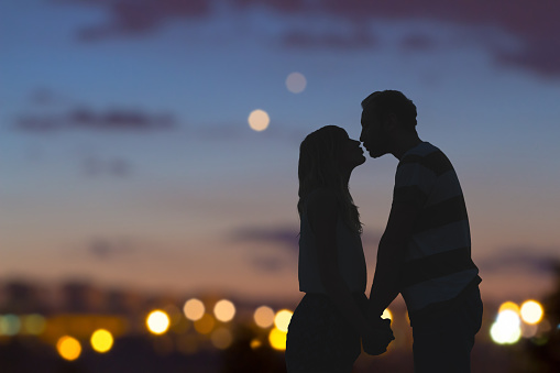 Siluetas de una pareja de jóvenes besándose con vista panorámica de la ciudad en el fondo. photo